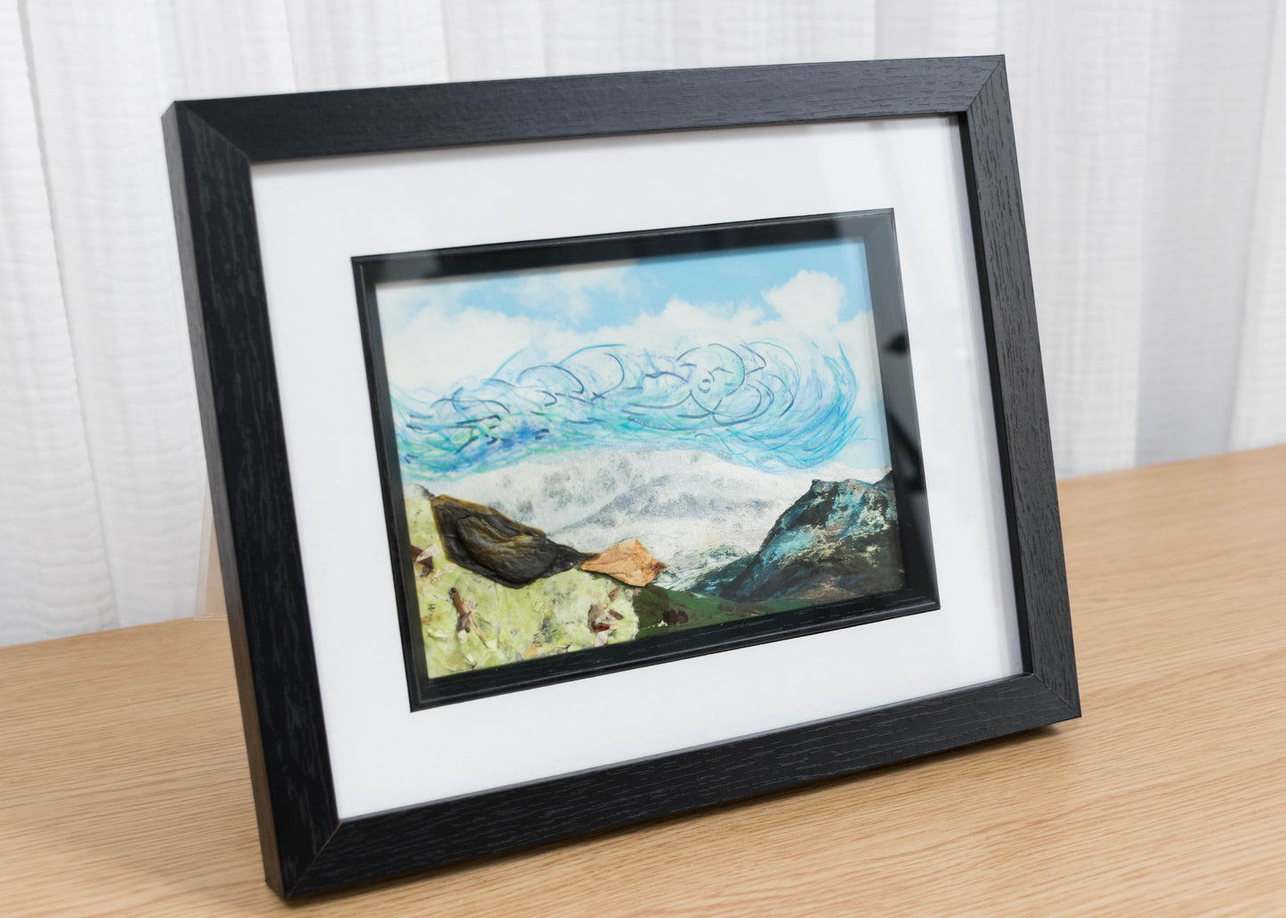 Framed artwork of a coastal scene with waves and rocks on a wooden surface.