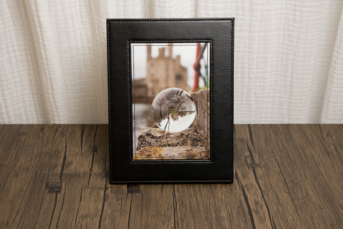 Framed photograph of landscape with a glass orb on a wooden surface with a white curtain background