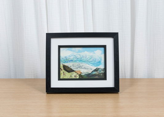 Framed artwork on a wooden surface with a white curtain background
