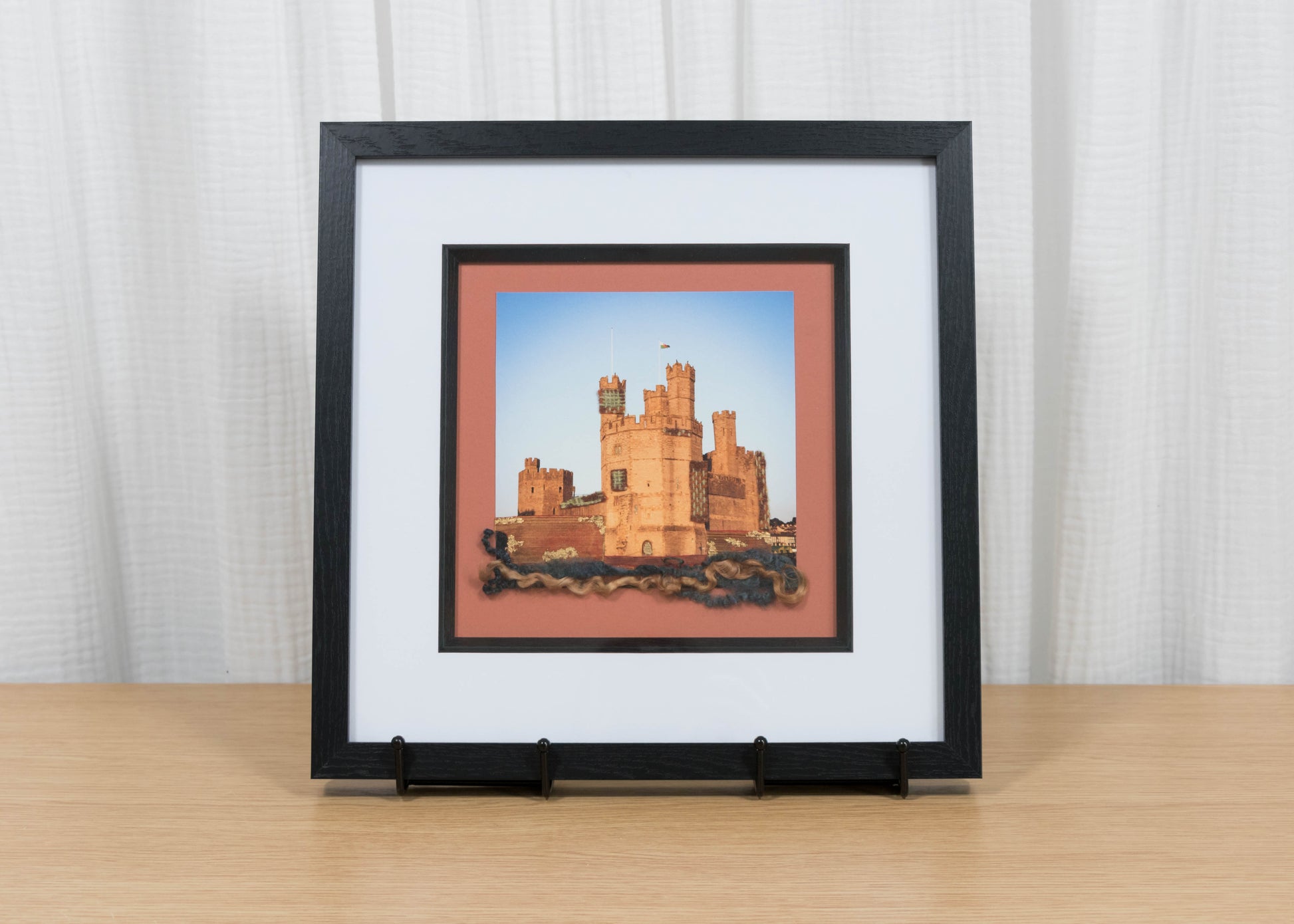 Framed artwork of a castle on a wooden surface with a white curtain background