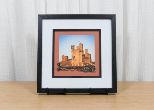Framed artwork of a castle on a wooden surface with a white curtain background