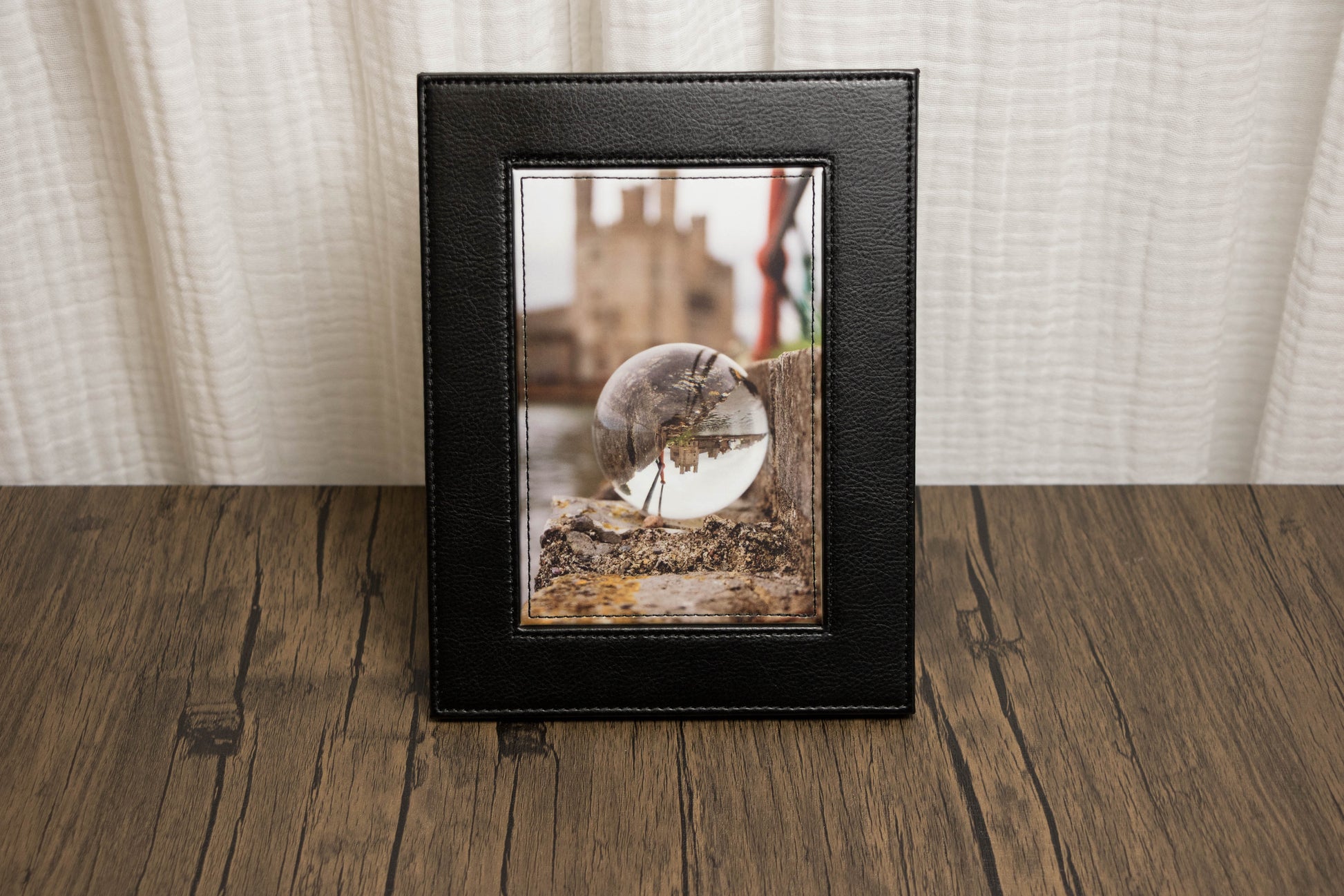 Framed photograph of landscape with a glass orb on a wooden surface with a white curtain background