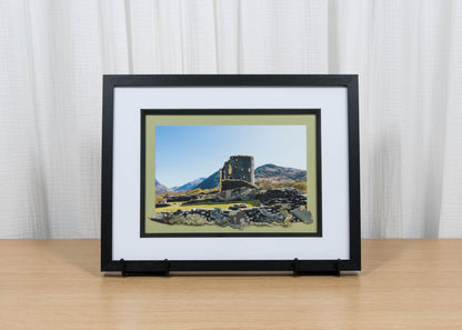 Framed artwork of a landscape with a castle on a wooden surface and white curtain background