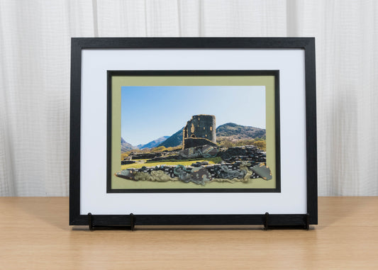 Framed artwork of a landscape with a castle on a wooden surface and white curtain background