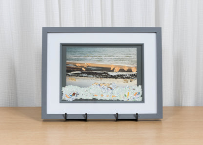 Framed artwork of a beach scene on a wooden surface with a white curtain background