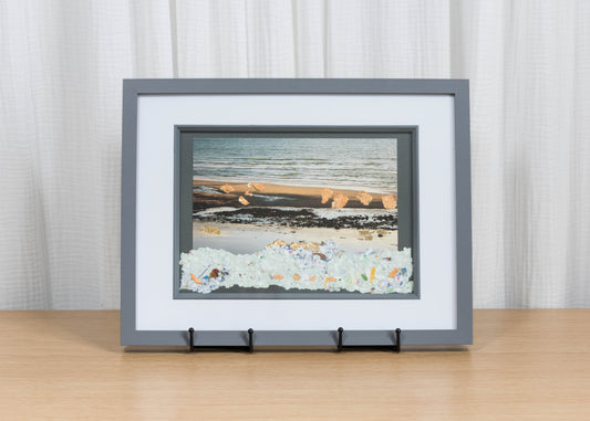 Framed artwork of a beach scene on a wooden surface with a white curtain background