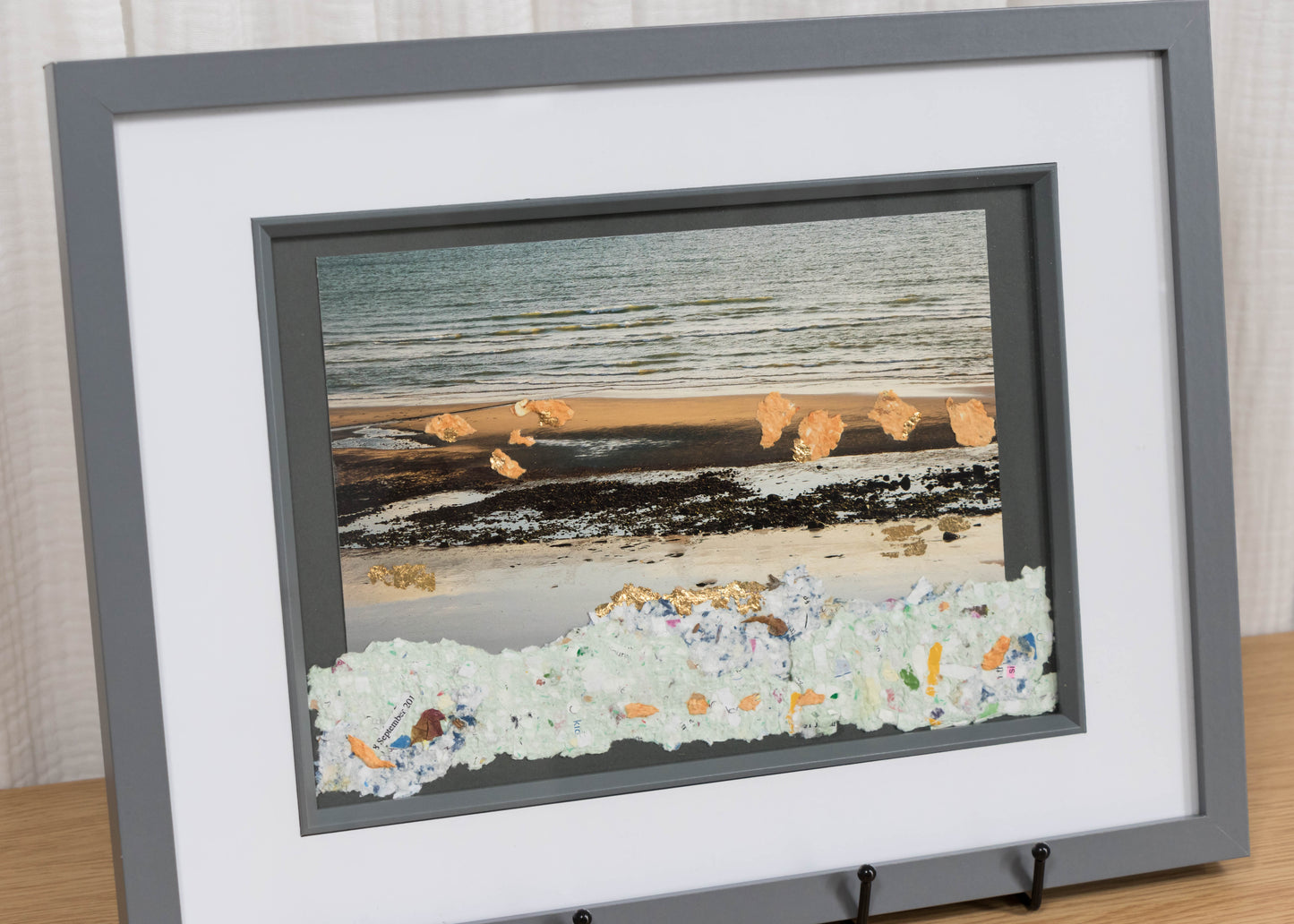 Framed artwork of a beach scene on a wooden surface with a white curtain background