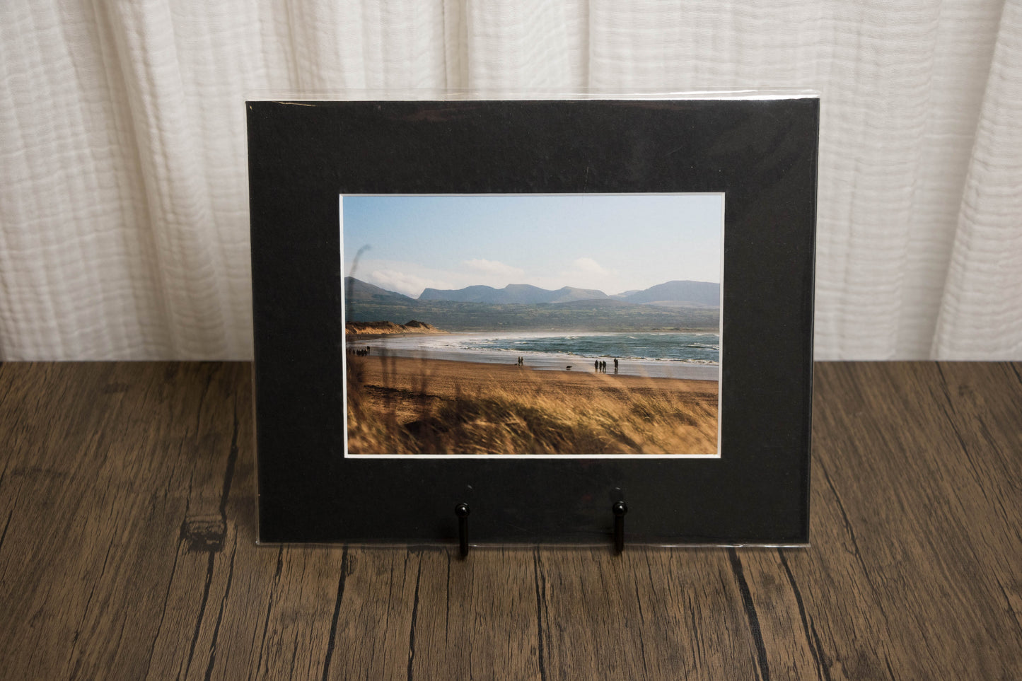 Framed photograph of a landscape with mountains and water on a wooden surface.