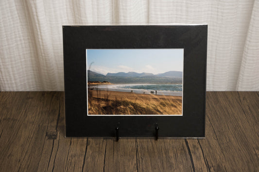 Framed photograph of a landscape with mountains and water on a wooden surface.